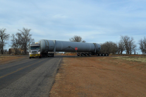 A removable gooseneck flatbed trailer makes a tight left turn while hauling an oversize load