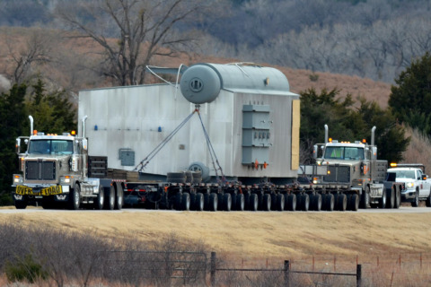 A hydraulic platform flatbed trailer hauls an oversize load with a pilot car following closely behind