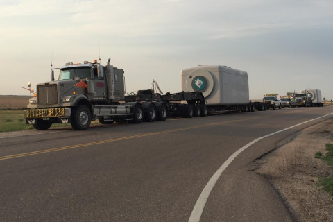 Two Parish Transport removable gooseneck flatbed trailers transport oversize loads with pilot cars in between them