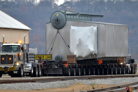 A hydraulic platform flatbed trailer hauls an oversize load alongside railroad tracks