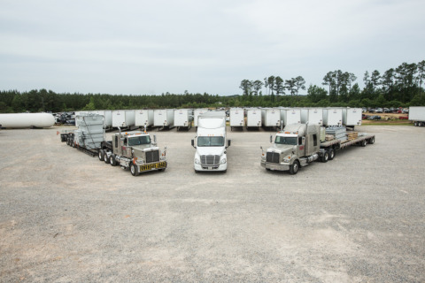 A removable gooseneck trailer, dry van semi-trailer, and an extendable drop deck flatbed trailer are parked in a lot